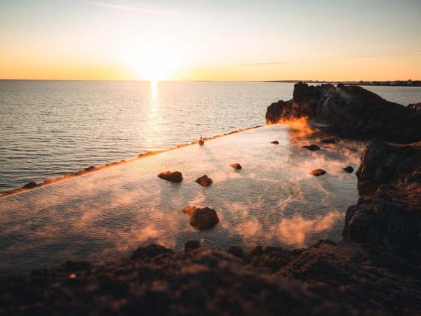 una persona está nadando en una piscina de agua caliente cerca del océano al atardecer.