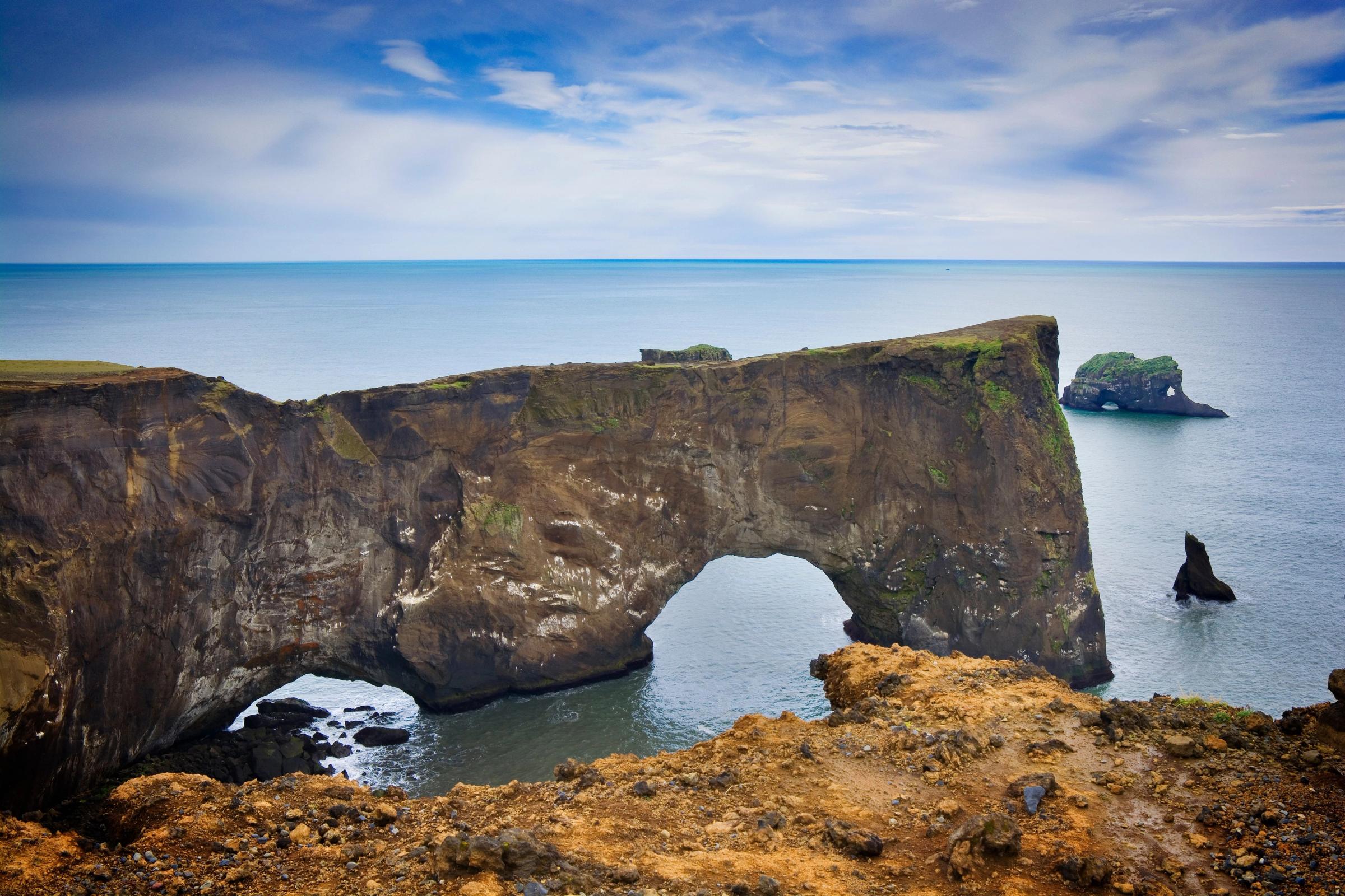 Natural rock arch extending into the ocean, with smaller rock stacks further out.