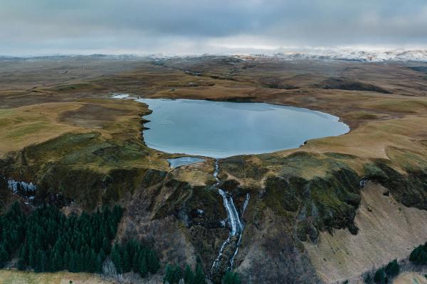 Aerial view of a lake in the middle of a vast landscape with snowy mountains in the background