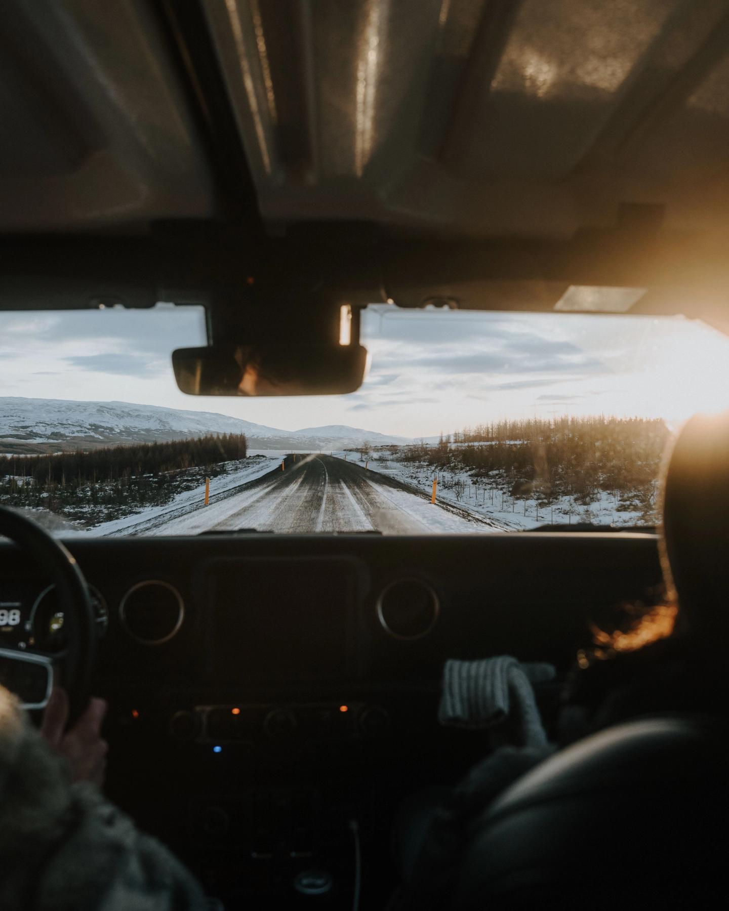 Vista desde el salpicadero de un coche conduciendo por una carretera nevada hacia un sol brillante.