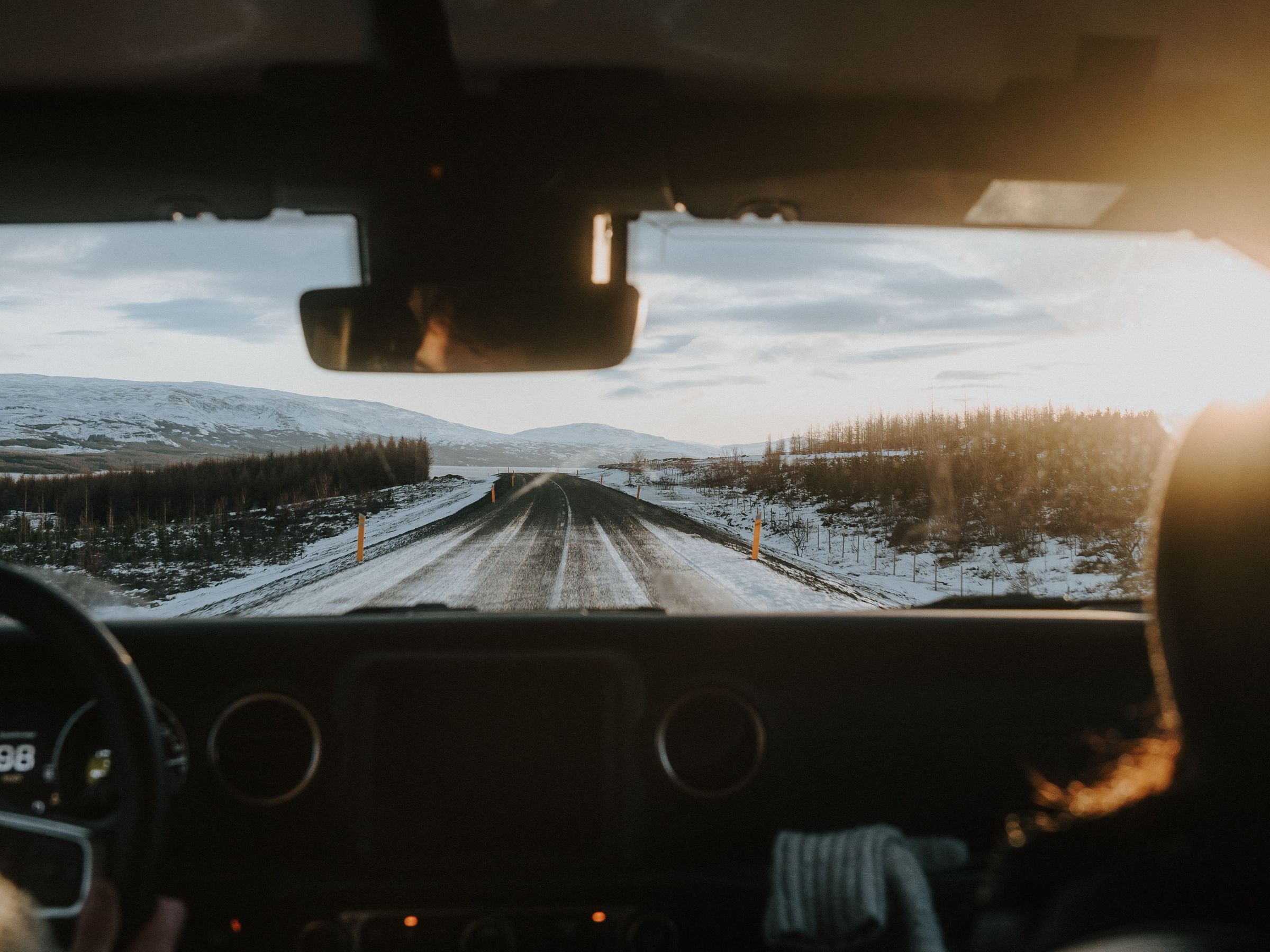Vista desde el salpicadero de un coche conduciendo por una carretera nevada hacia un sol brillante.