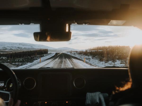 Vista desde el salpicadero de un coche conduciendo por una carretera nevada hacia un sol brillante.