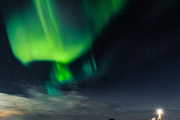 White lighthouse on a coastline at sunset, with water in the foreground.