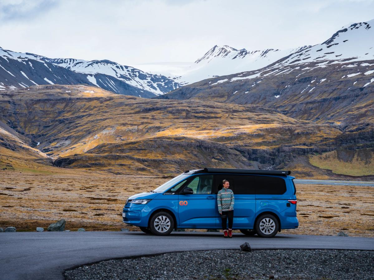 Camping-car Mountain Valley Personne à côté du camping-car sur une route goudronnée dans une vallée montagneuse, location de camping-car 4x4 en Islande