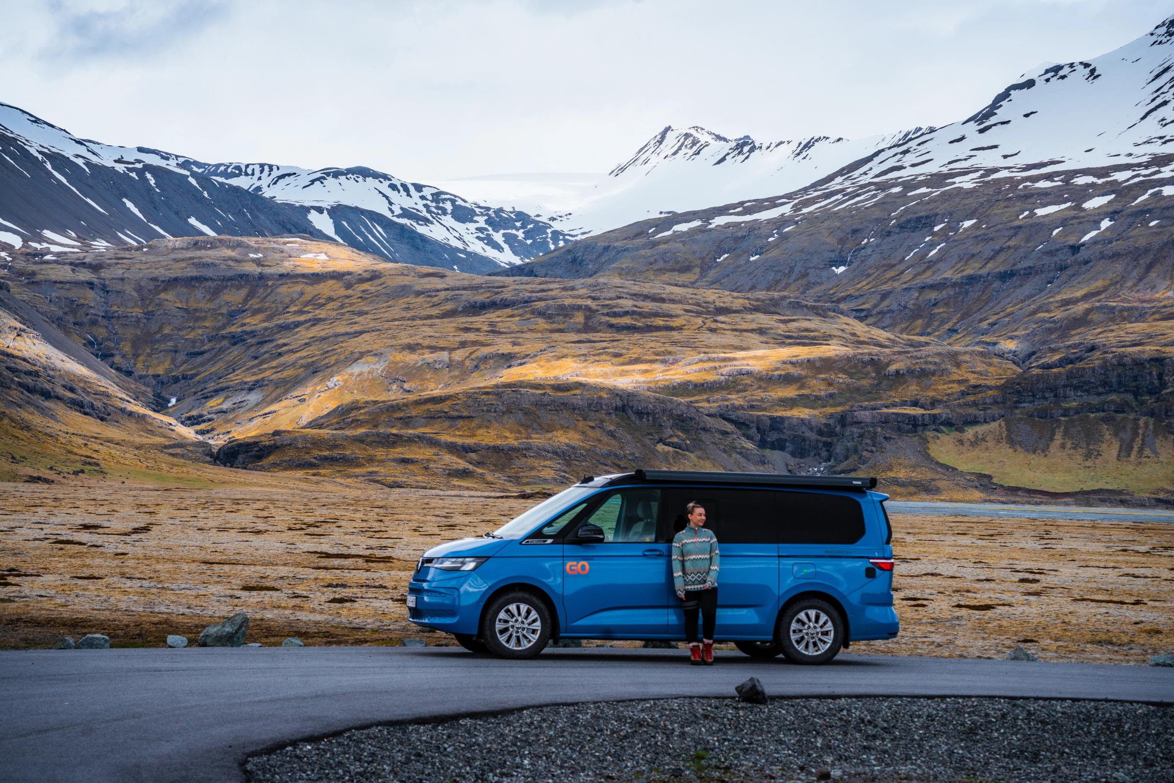 Camping-car Mountain Valley Personne à côté du camping-car sur une route goudronnée dans une vallée montagneuse, location de camping-car 4x4 en Islande