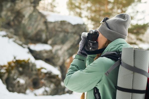 A person in winter clothing photographs a snowy, rocky landscape.