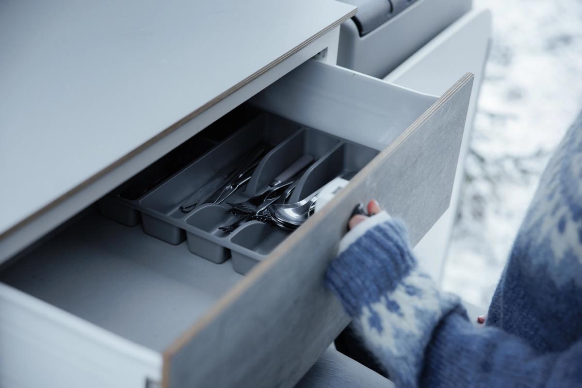 Geöffnete Küchenschublade mit einem grauen Besteckeinsatz, in dem Gabeln, Messer und Löffel liegen