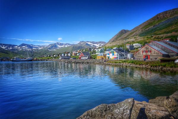 a small town is sitting next to a body of water with mountains in the background at siglufjordur in iceland. .