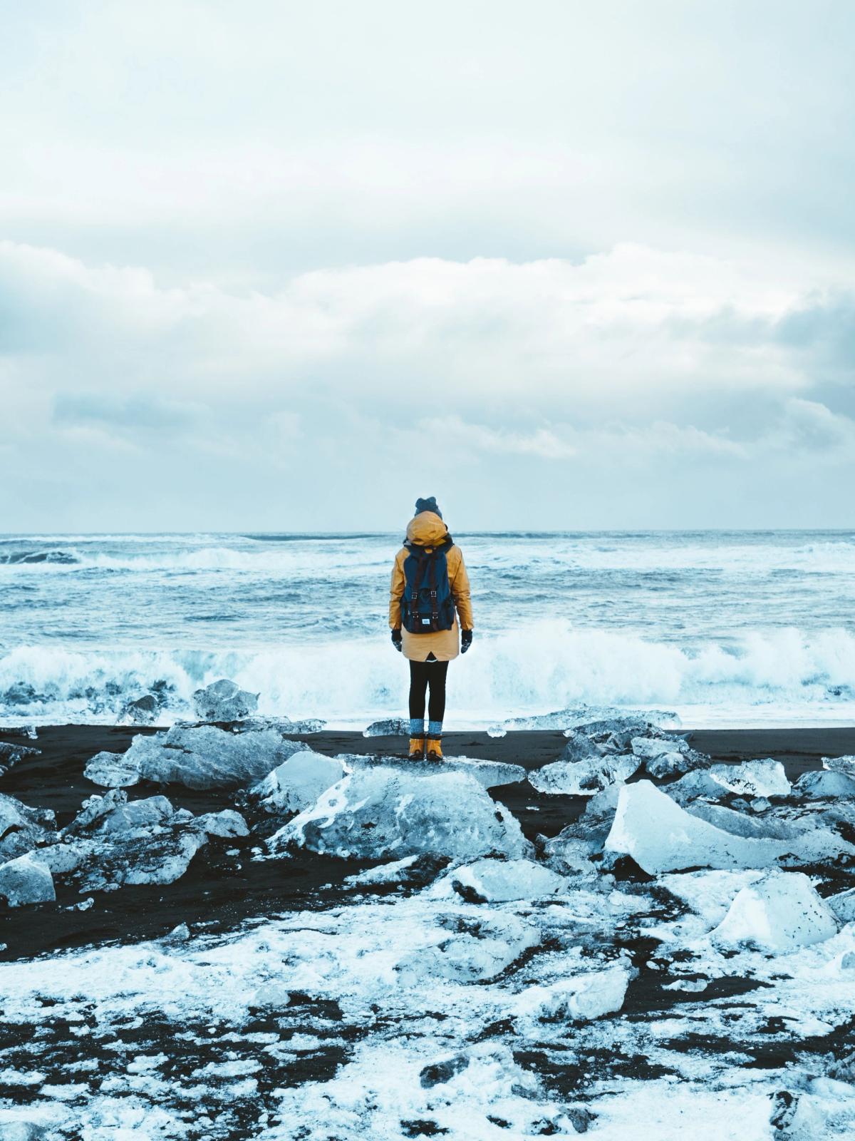 Chica mirando al mar en la orilla de la Diamond Beach con trozos de hielo detrás de ella