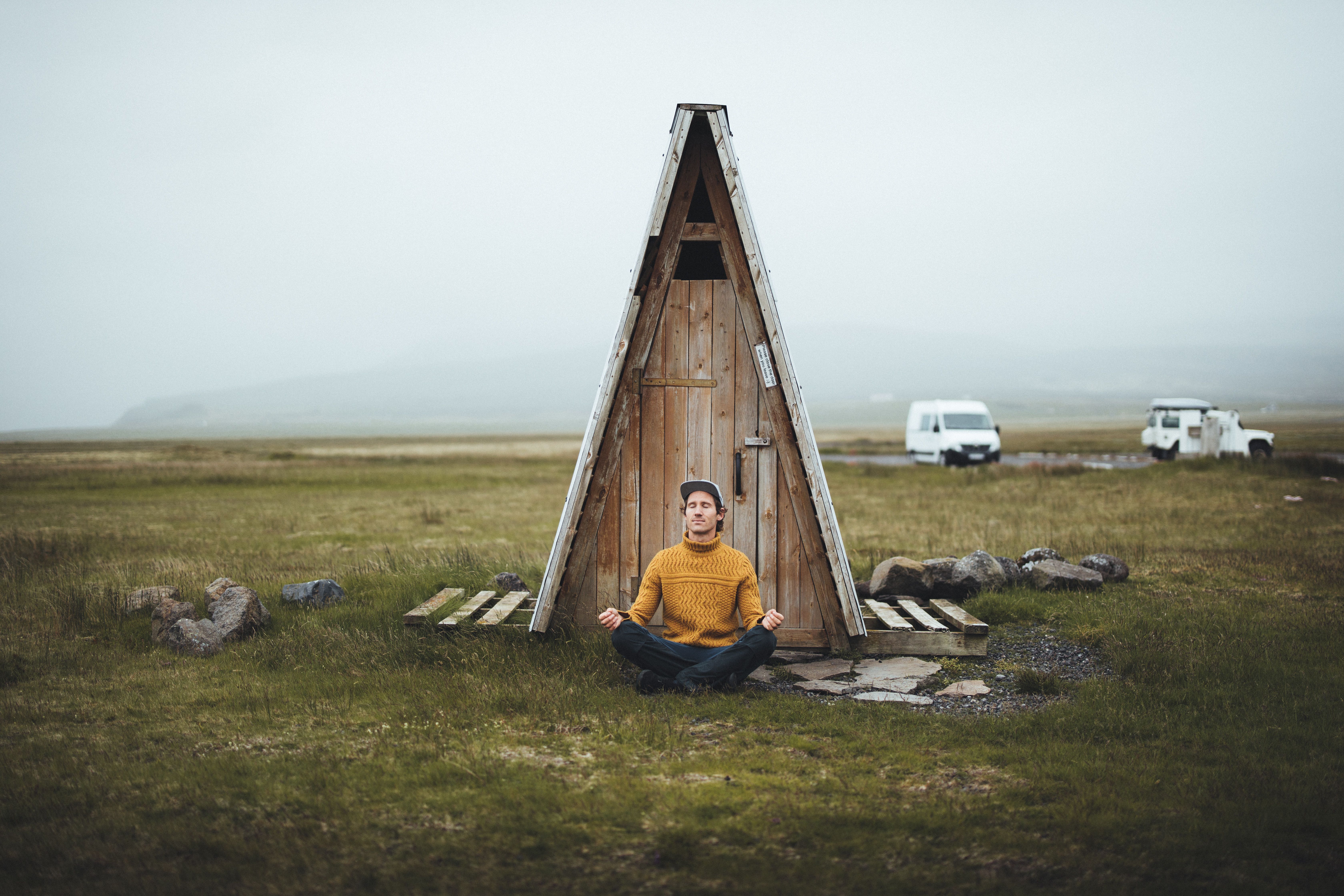 a man is sitting in a lotus position in front of a wooden outhouse .
