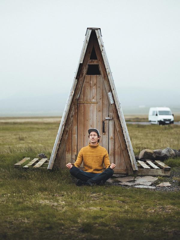 a man is sitting in a lotus position in front of a wooden outhouse .