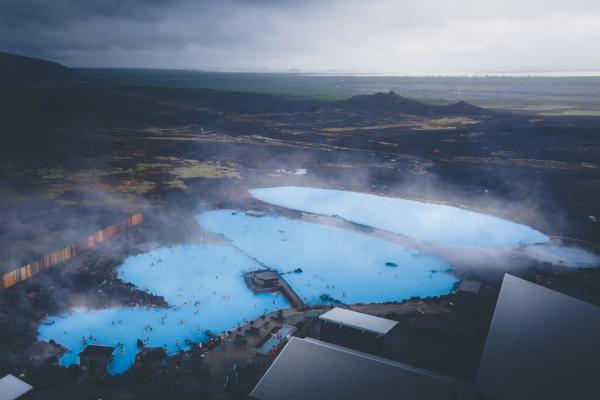 Aerial view of Mývatn Nature Baths with steaming blue geothermal pools surrounded by dark volcanic terrain in northern Iceland.