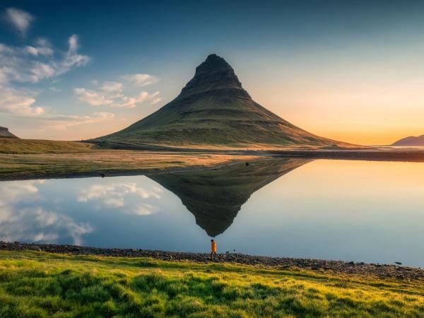 a person is standing on the shore of a lake with a mountain reflected in the water .