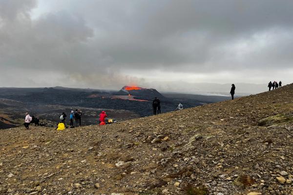 a group of people are standing on top of a rocky hill looking at a volcano .
