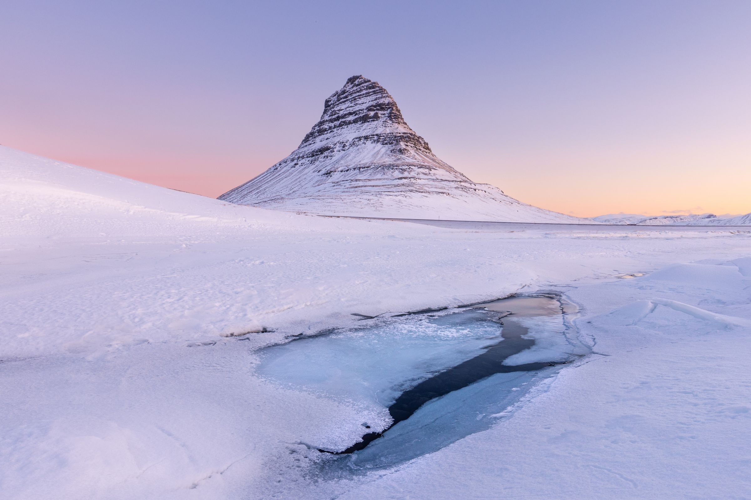 une montagne couverte de neige et de glace avec un ruisseau qui la traverse au mont Kirkufell, dans la péninsule de Snæfellsnes en Islande.
