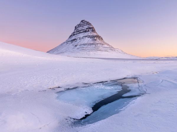 une montagne couverte de neige et de glace avec un ruisseau qui la traverse au mont Kirkufell, dans la péninsule de Snæfellsnes en Islande.