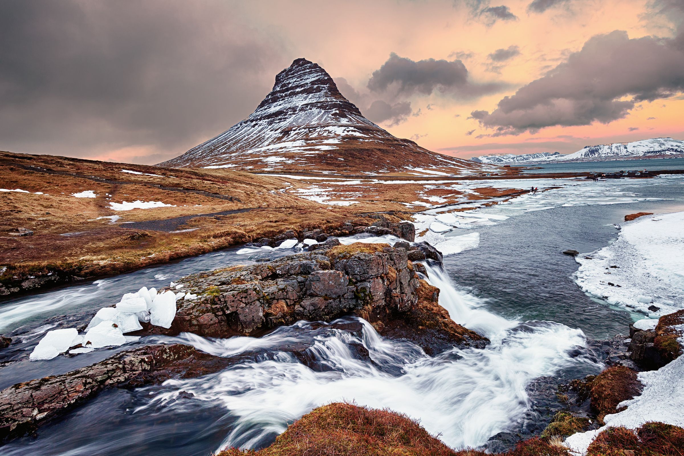 Une montagne couverte de neige est entourée par une rivière et une cascade au mont Kirkufell, dans la péninsule de Snæfellsnes en Islande.