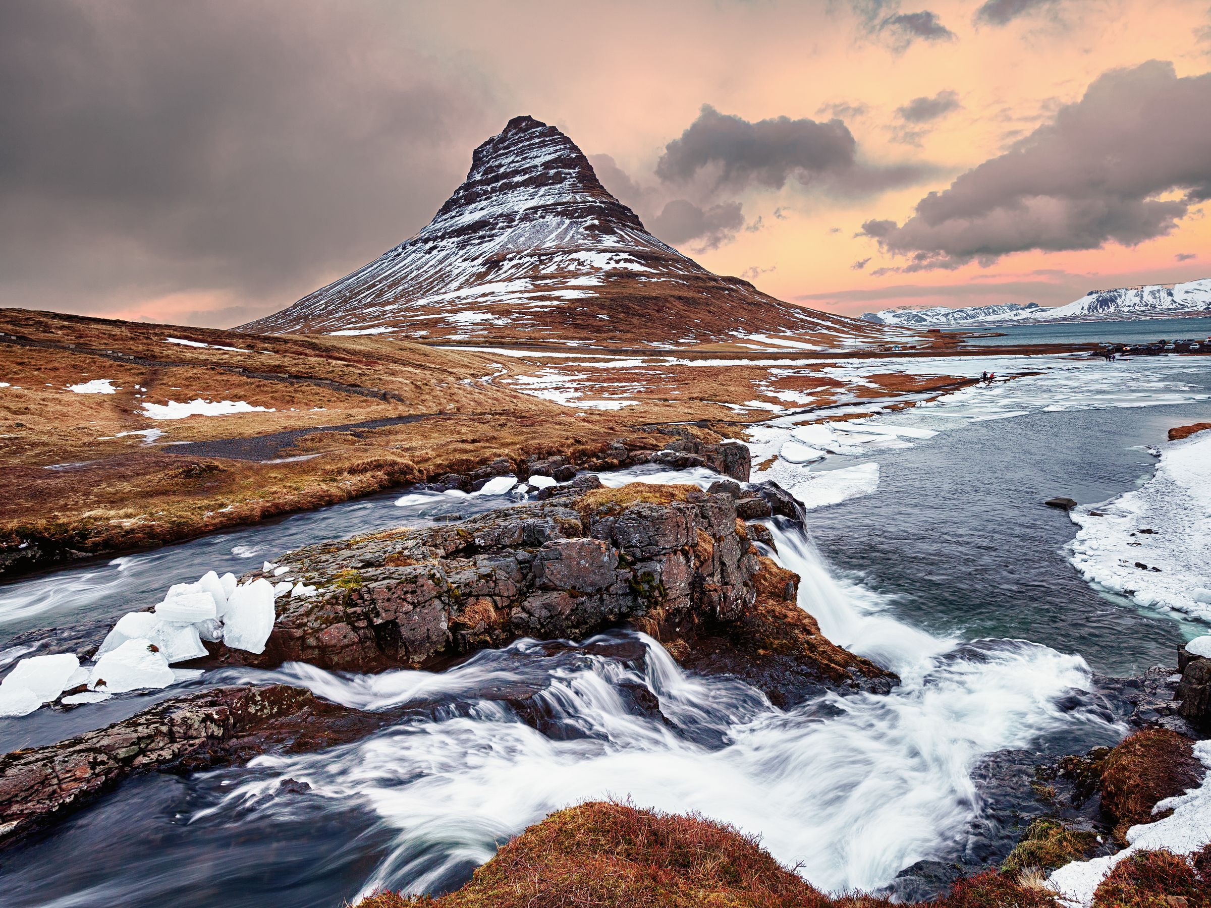 Une montagne couverte de neige est entourée par une rivière et une cascade au mont Kirkufell, dans la péninsule de Snæfellsnes en Islande.