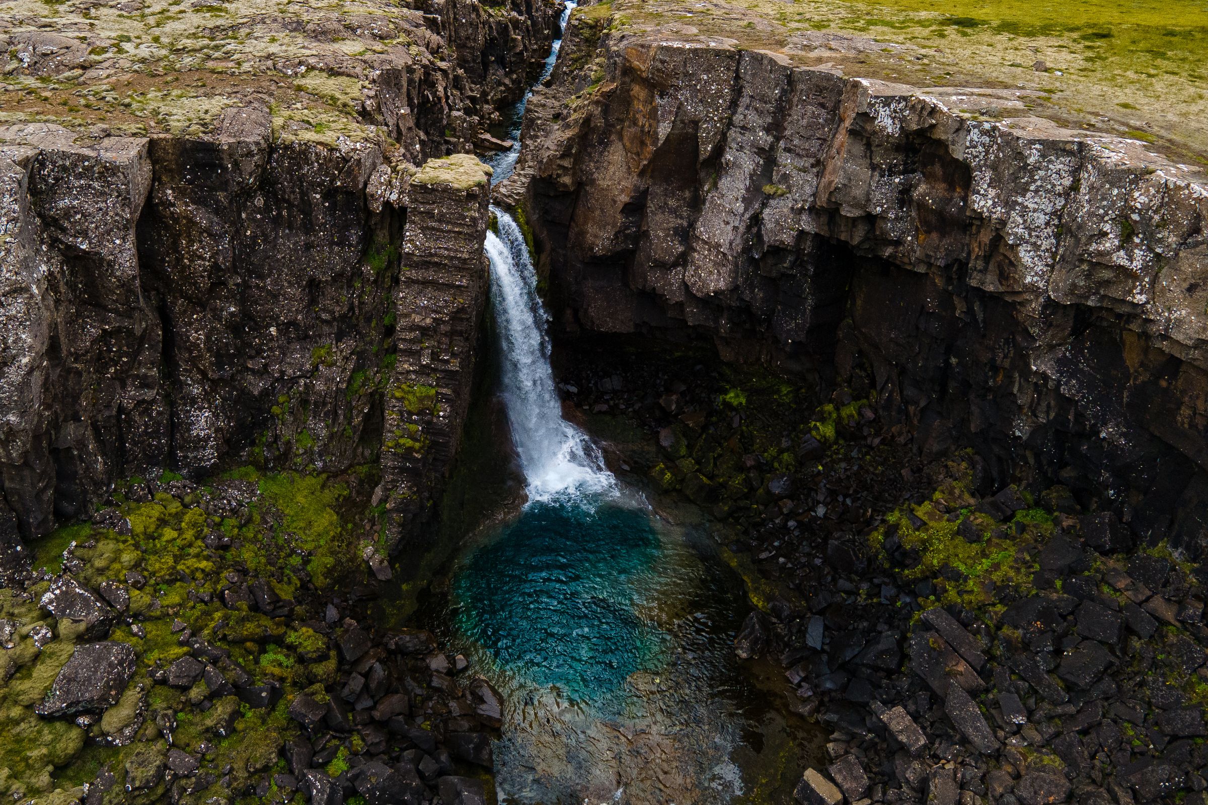 A waterfall cascades into a vivid blue pool surrounded by dark, mossy rock cliffs.