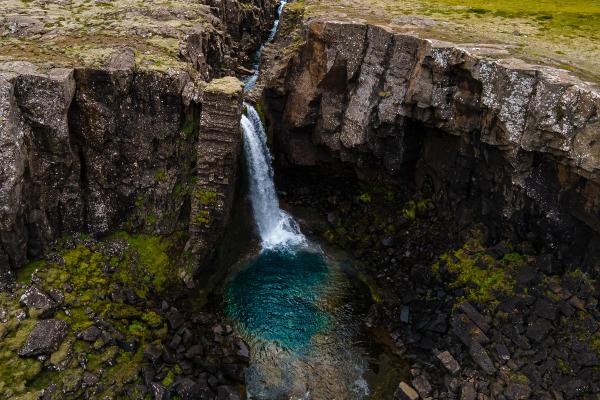 A waterfall cascades into a vivid blue pool surrounded by dark, mossy rock cliffs.