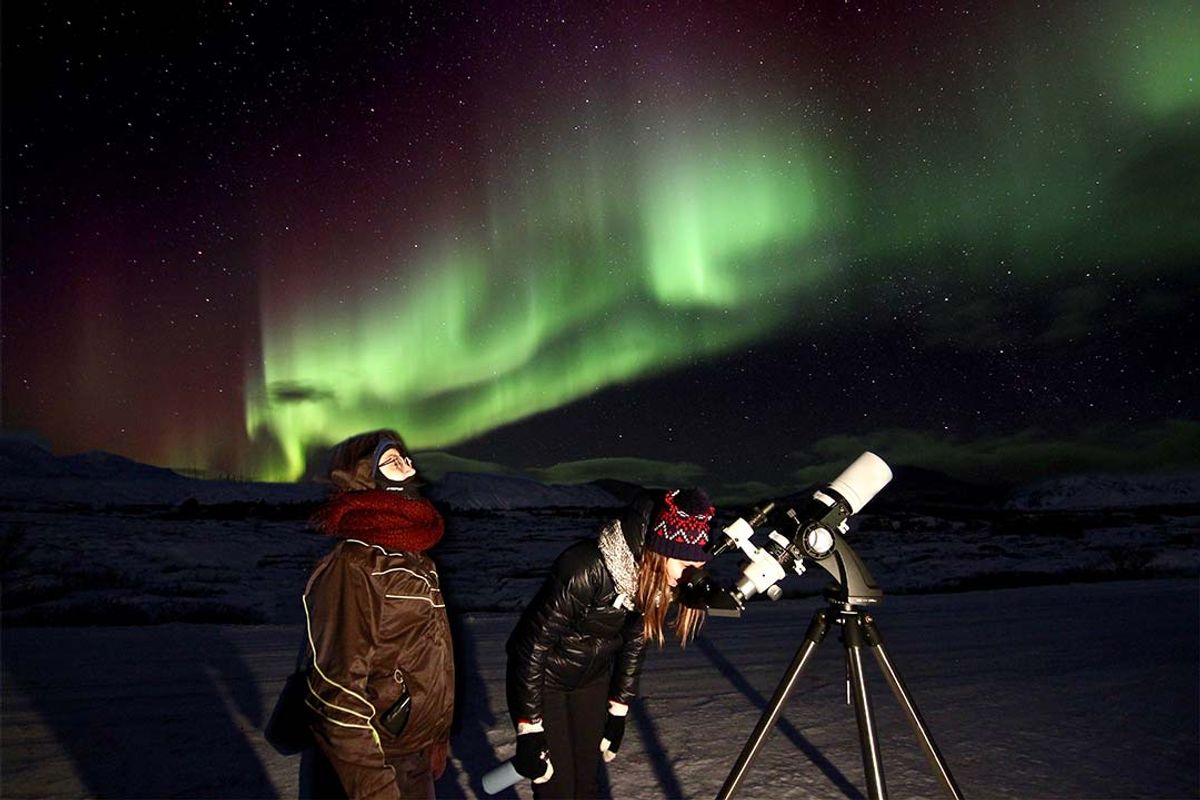 Dos personas miran la aurora boreal a través de un telescopio.