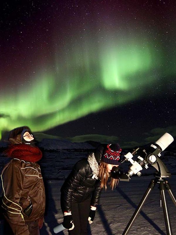 Dos personas miran la aurora boreal a través de un telescopio.