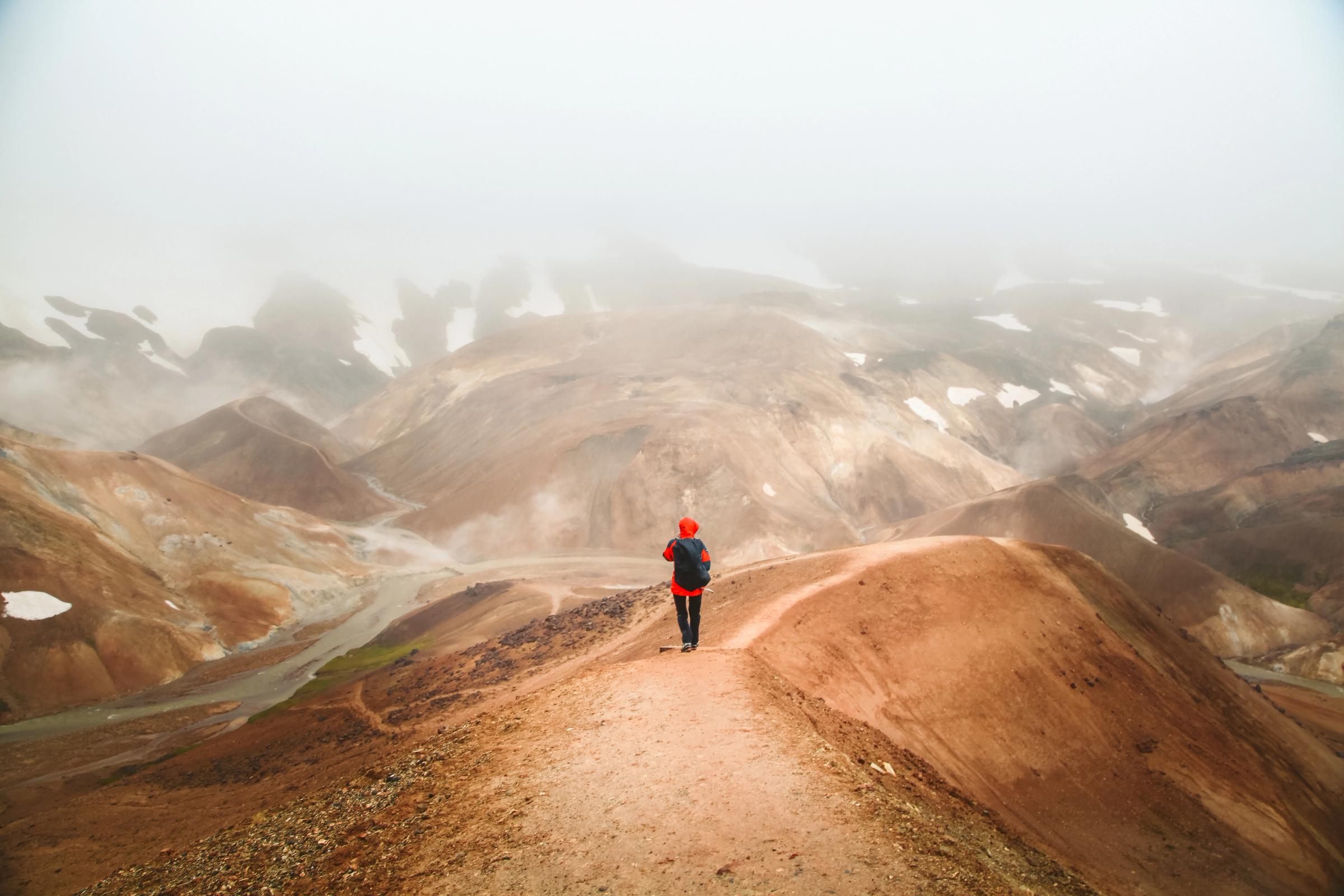 a person with a red jacket walking over brown hills