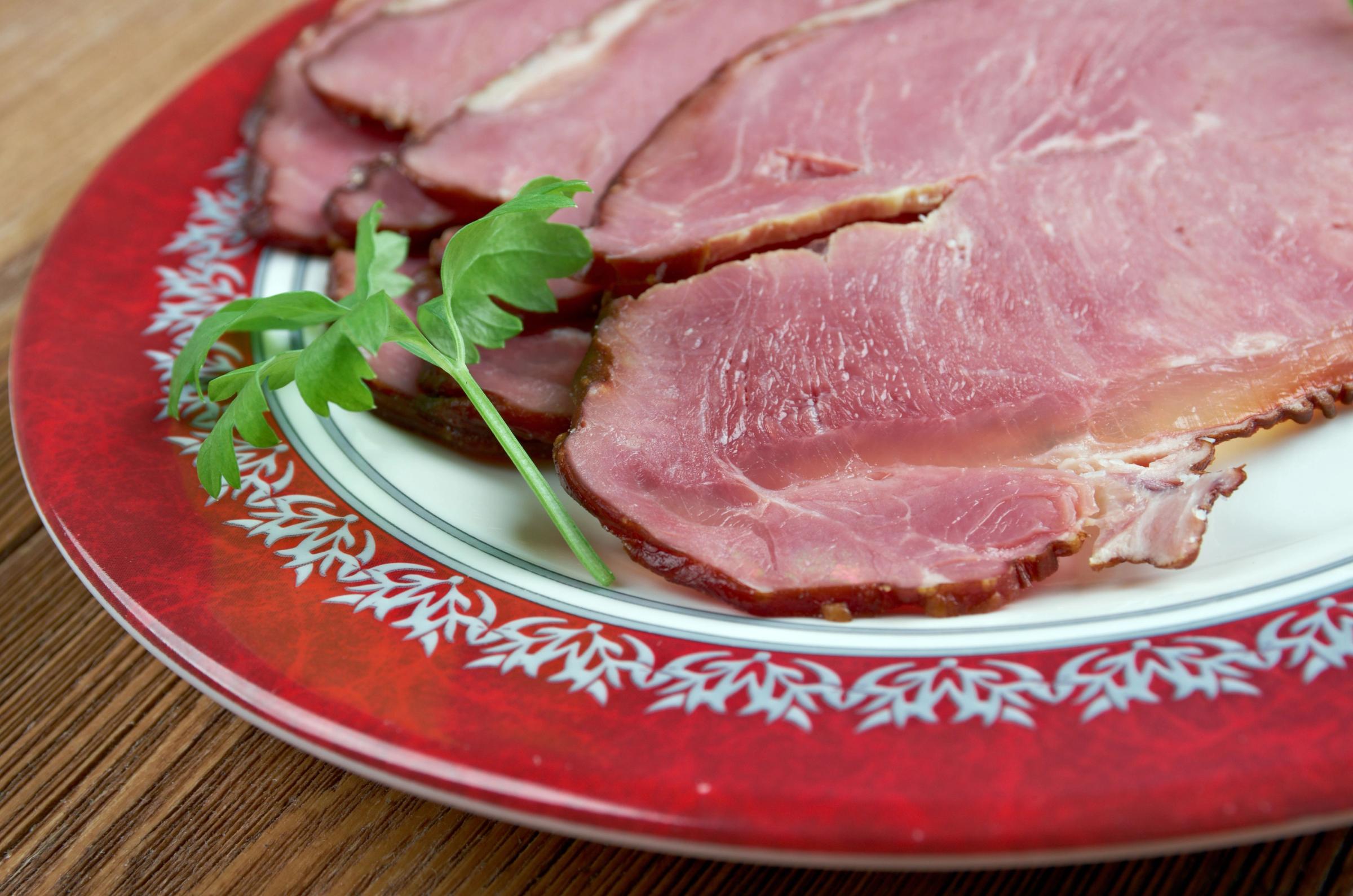 a plate of sliced ham with parsley on a wooden table .