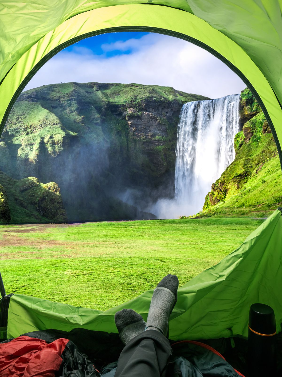 a person is laying in a tent with their feet up in front of a waterfall .