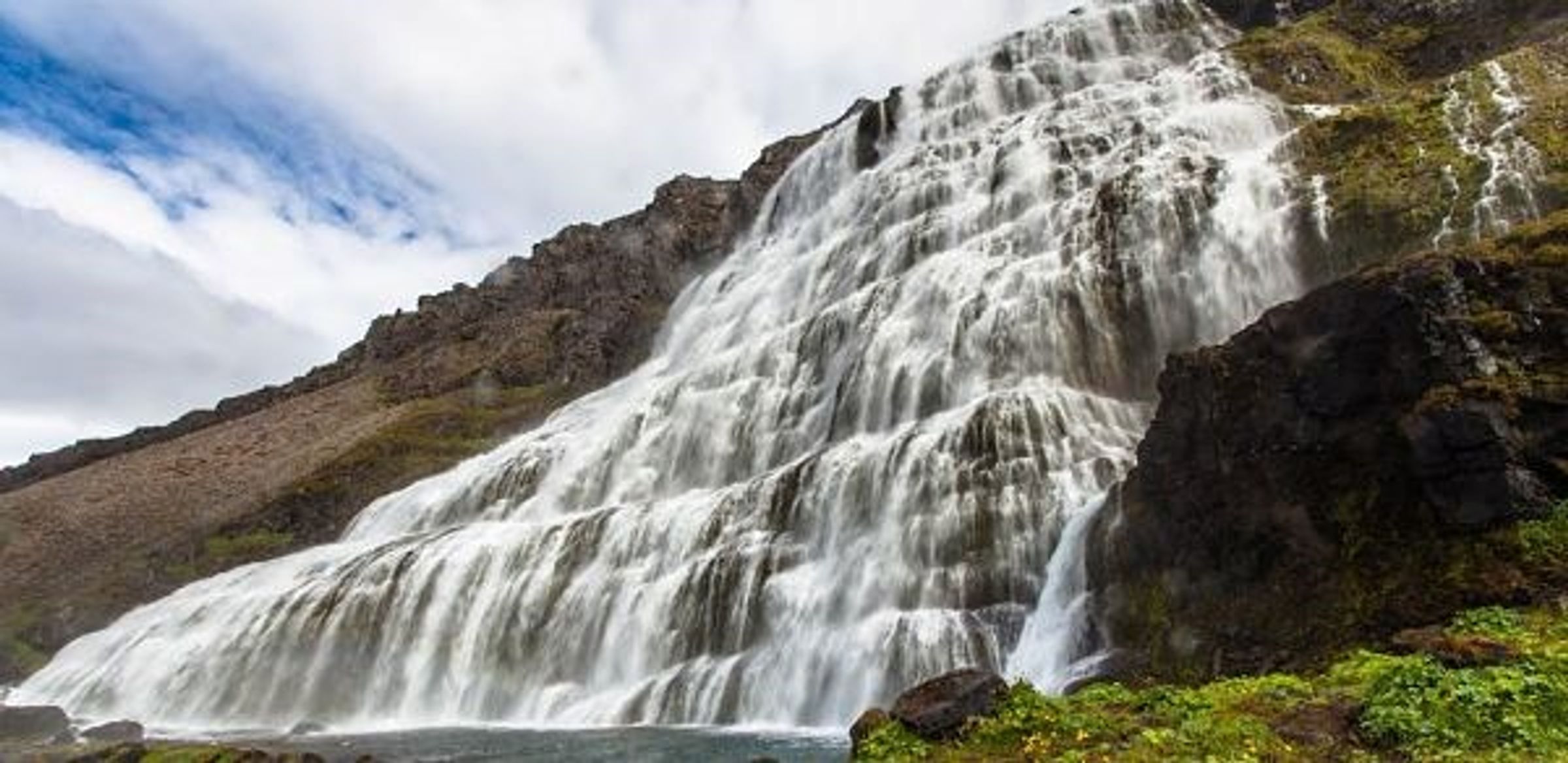 a waterfall is surrounded by rocks and grass on the side of a mountain .