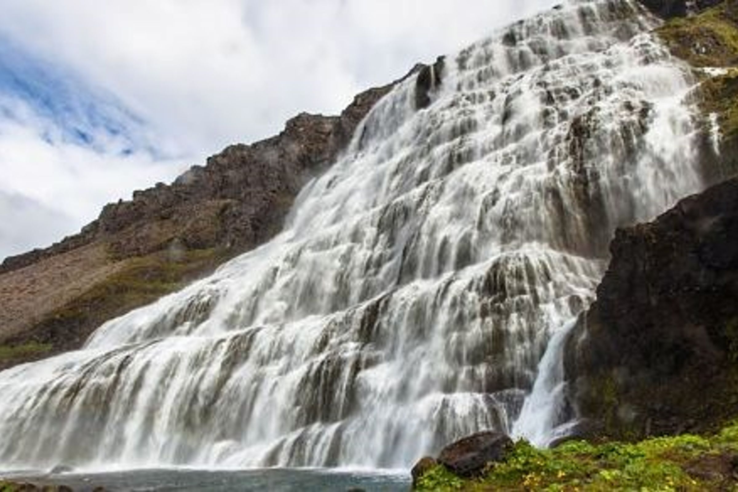 una cascada está rodeada de rocas y hierba en el costado de una montaña.