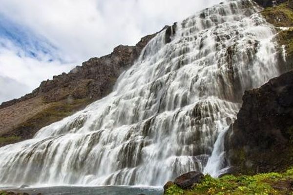 a waterfall is surrounded by rocks and grass on the side of a mountain .