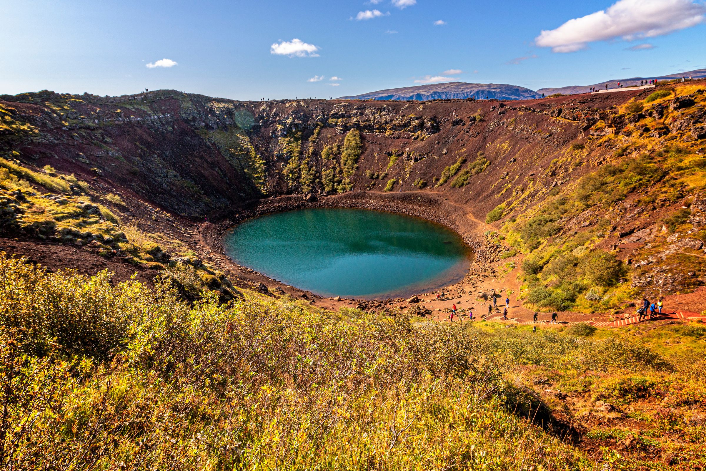 hay un gran lago en medio de un cráter rodeado de hierba y rocas.