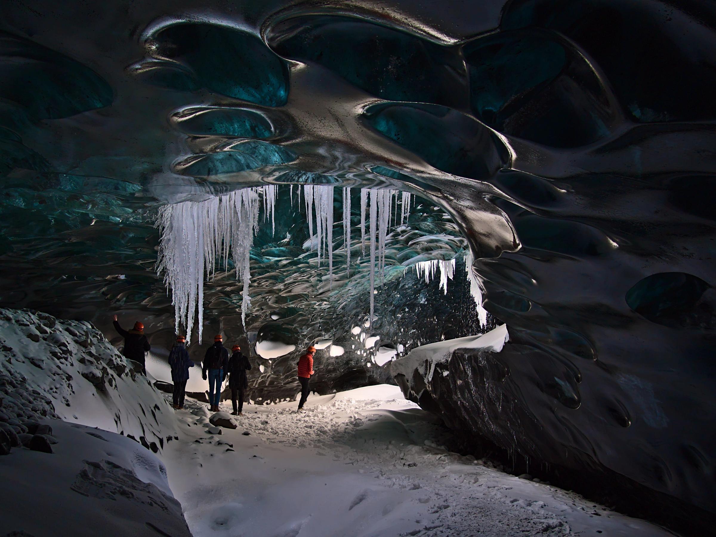 a group of people are standing inside of an ice cave with icicles hanging from the ceiling .