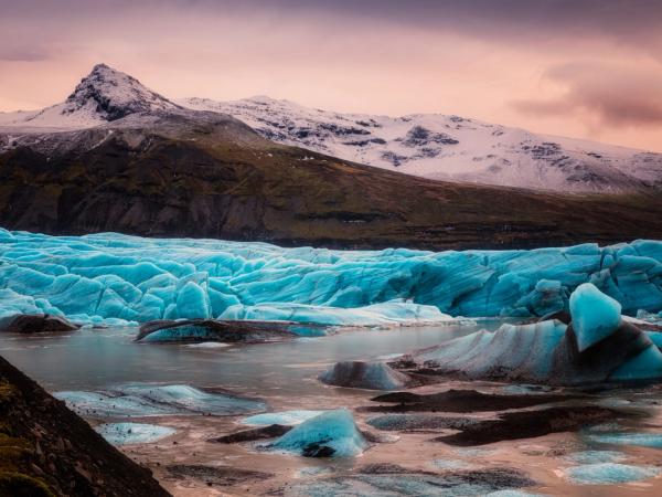 a large iceberg is melting into a lake with mountains in the background in iceland midnight sun.