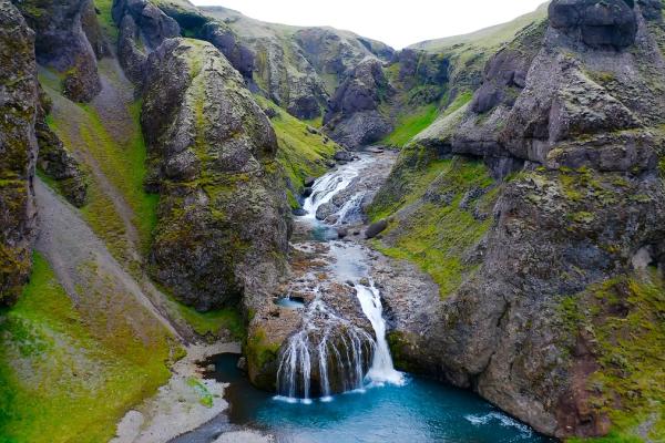 A river with multiple waterfalls winds through a lush green canyon.