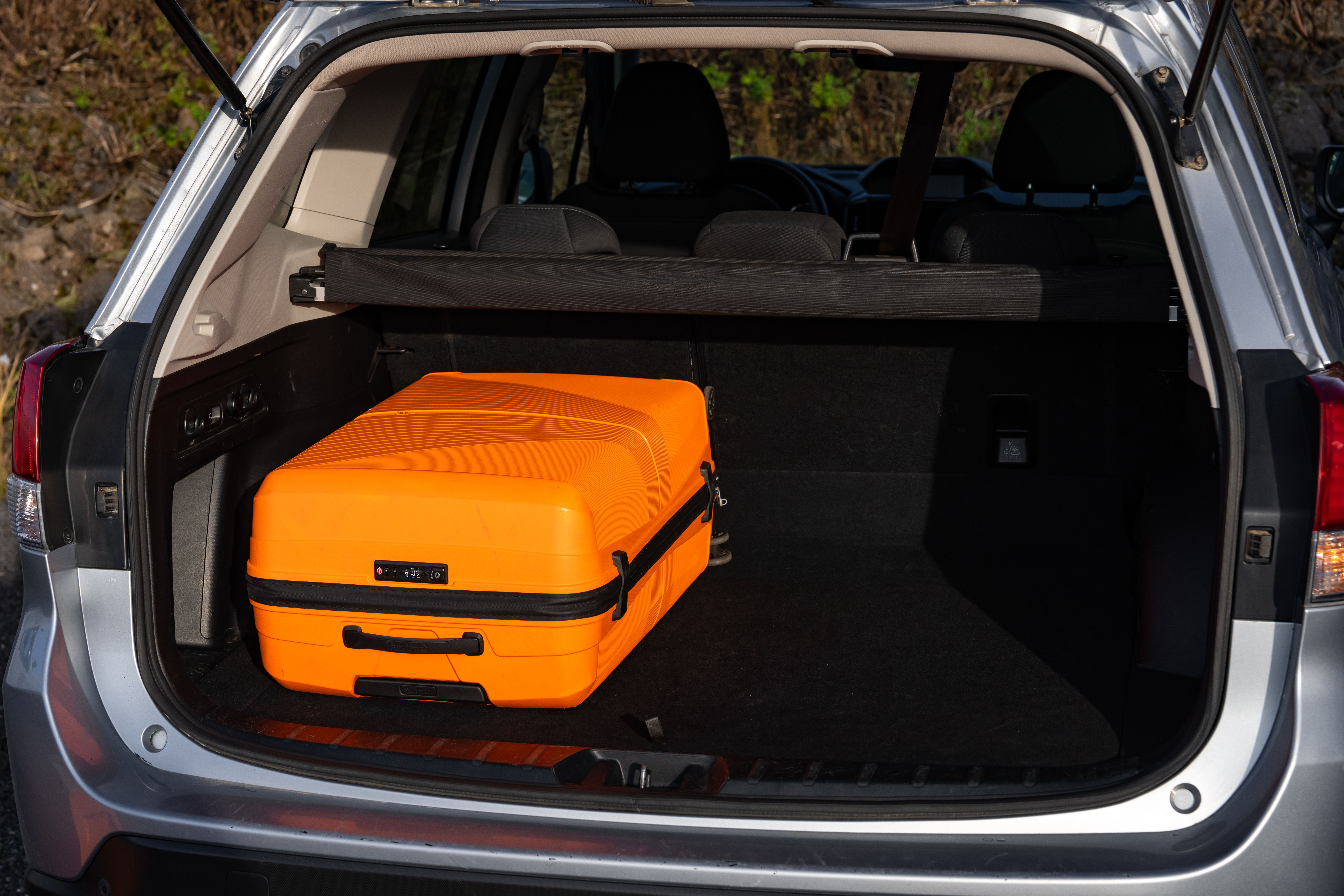 An orange suitcase sits in a car's dark trunk.