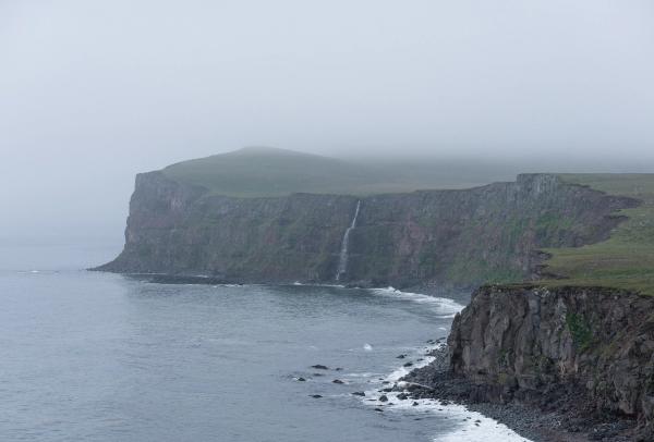 there is a waterfall on the cliff near the ocean .