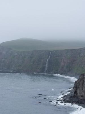 there is a waterfall on the cliff near the ocean .