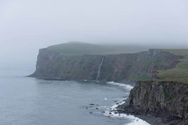 there is a waterfall on the cliff near the ocean at langanes in iceland.