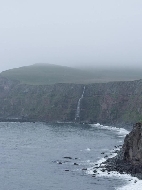 there is a waterfall on the cliff near the ocean .