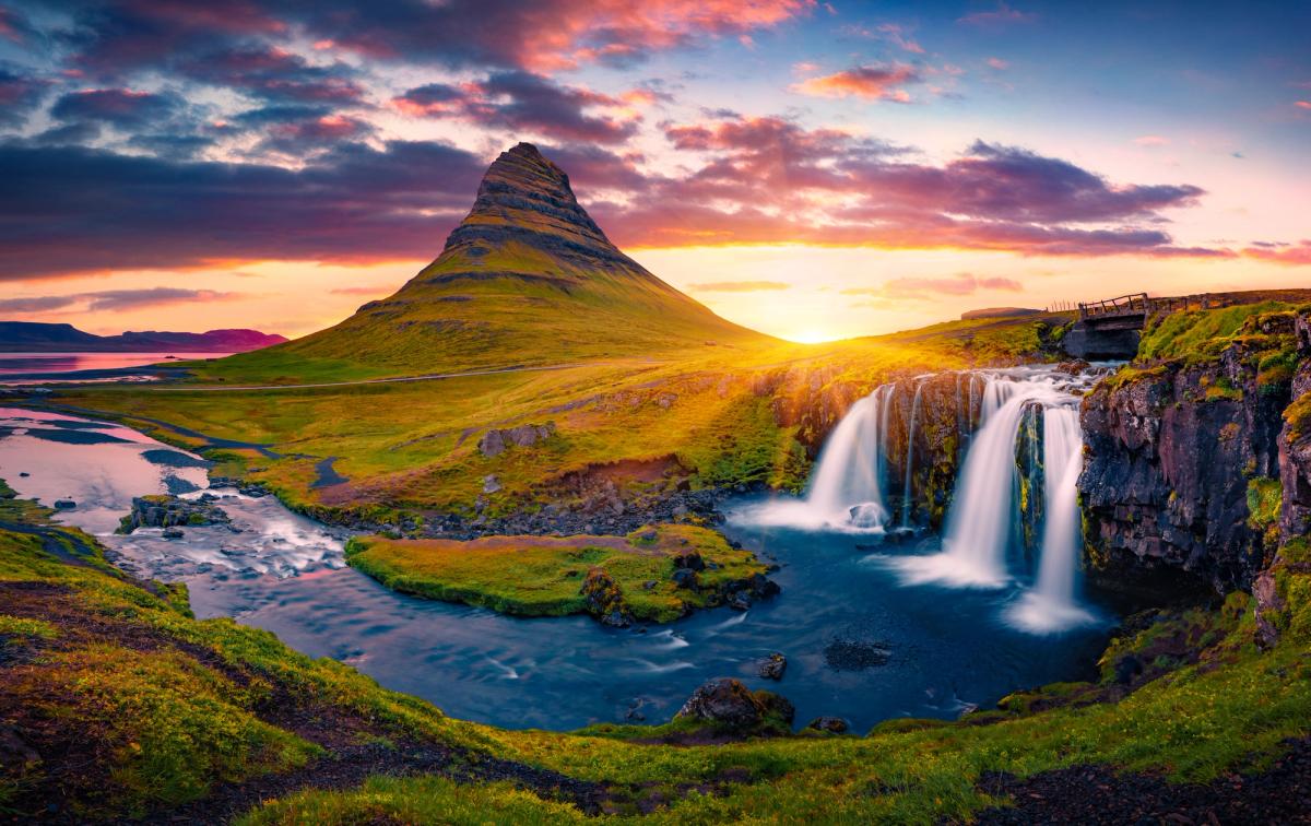 una cascada con una montaña al fondo al atardecer.