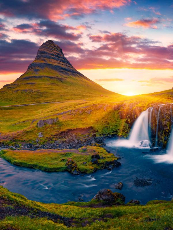 una cascada con una montaña al fondo al atardecer.