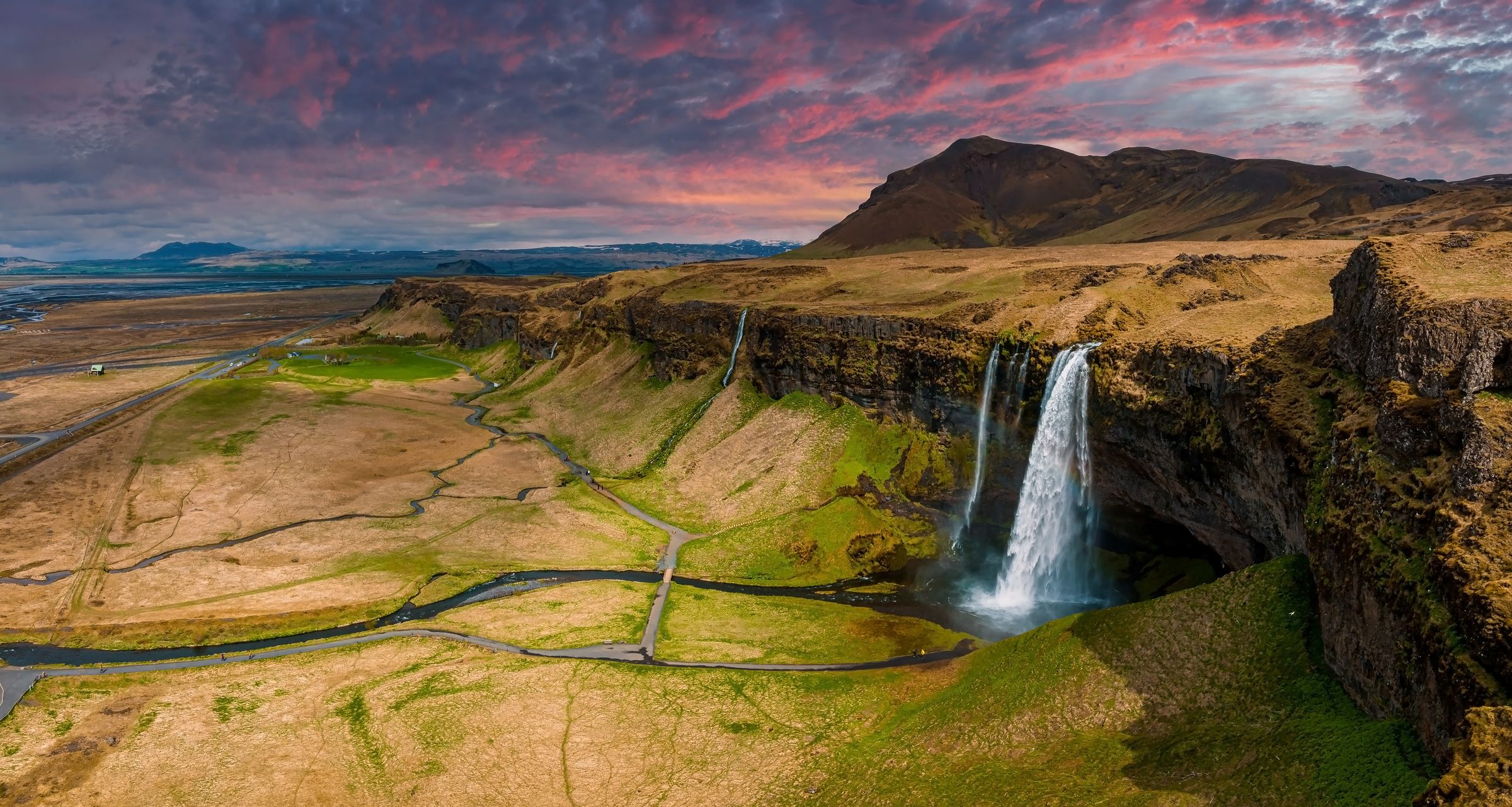 waterfall falling from a cliff with dried grass fields around it