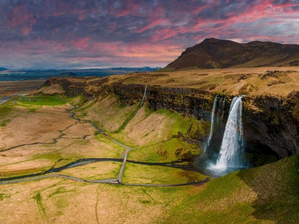 waterfall falling from a cliff with dried grass fields around it