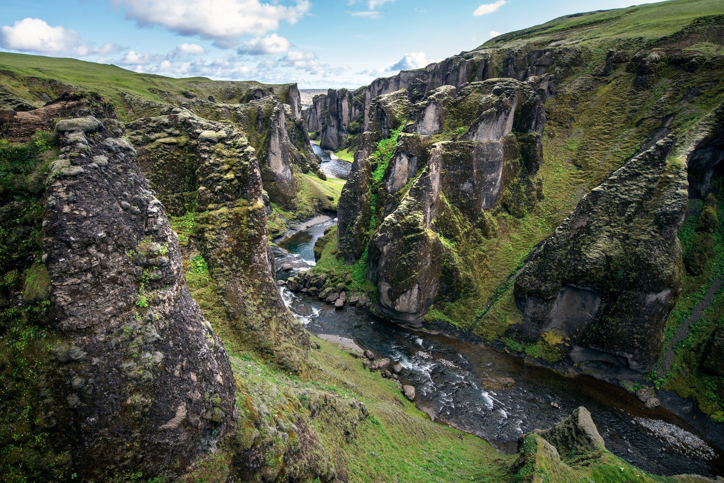 a river running through a canyon surrounded by rocks and grass at Fjaðrárgljúfur canyon in south east iceland.