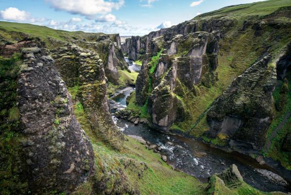a river running through a canyon surrounded by rocks and grass at Fjaðrárgljúfur canyon in south east iceland.