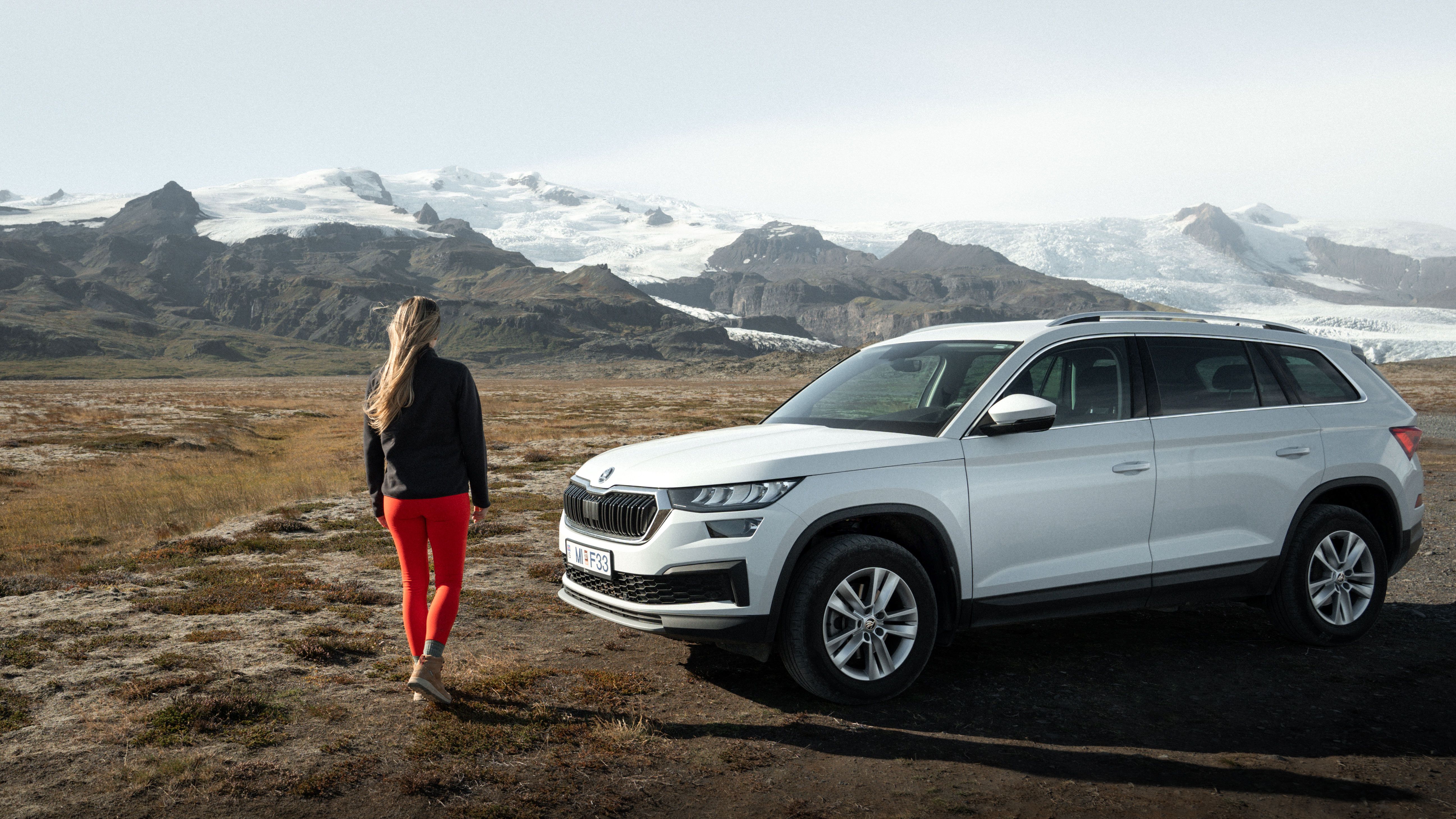 a woman is standing next to a white suv in a field .