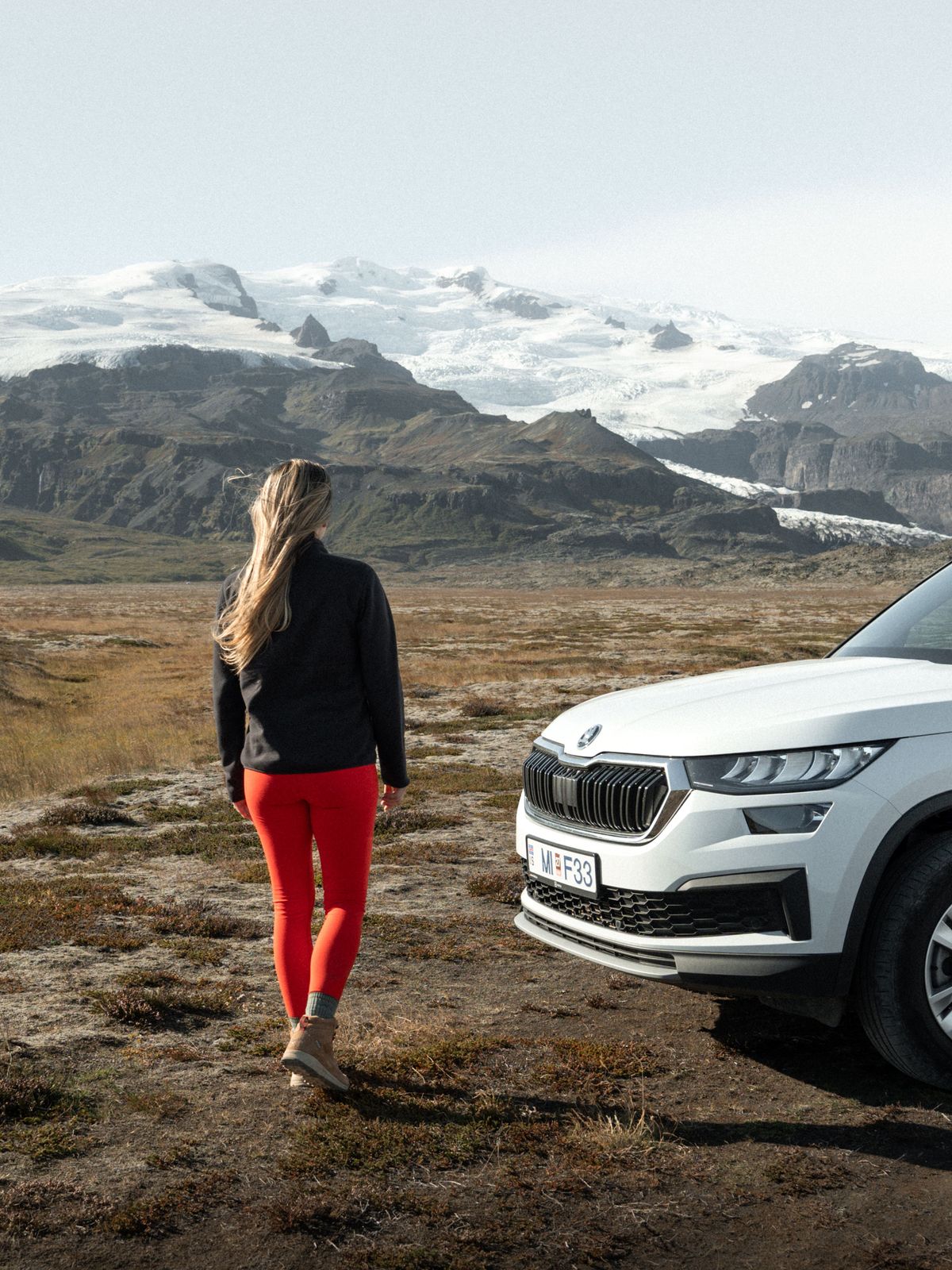 a woman is standing next to a white suv in a field .