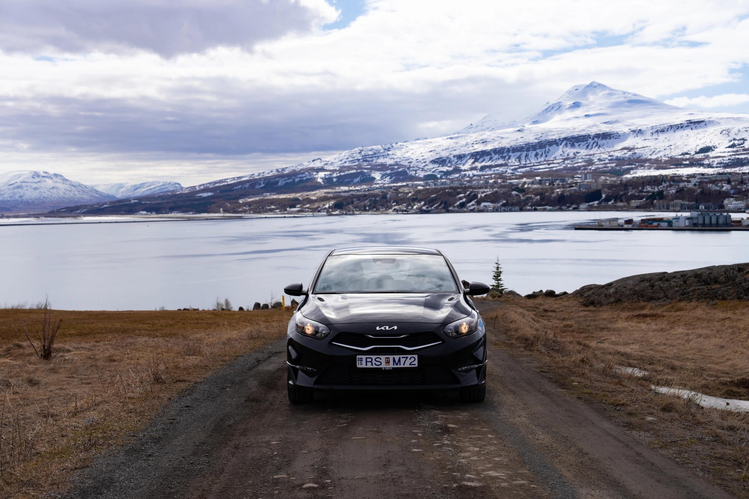 Kia Ceed self drive Iceland rental parked on gravel road beside a fjord
